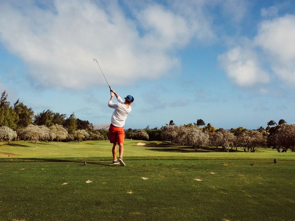 A golfer mid-swing driving a ball off the tee