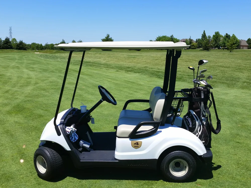 A golf cart on a path beside a fairway on a golf course