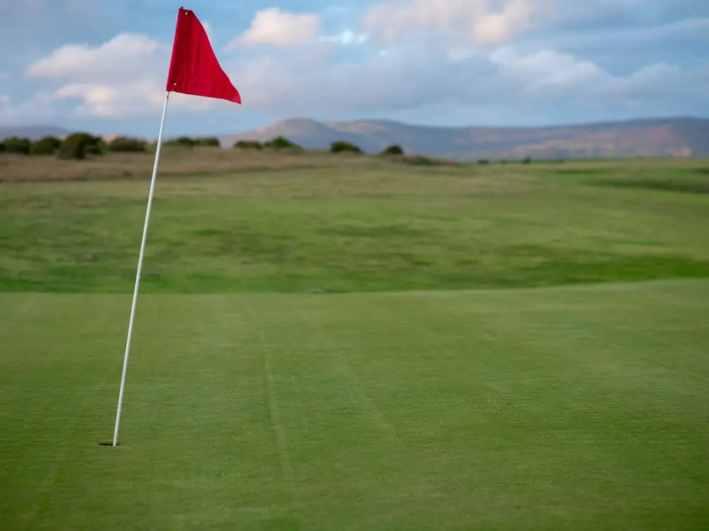 A golf green with a red flag on a clear day